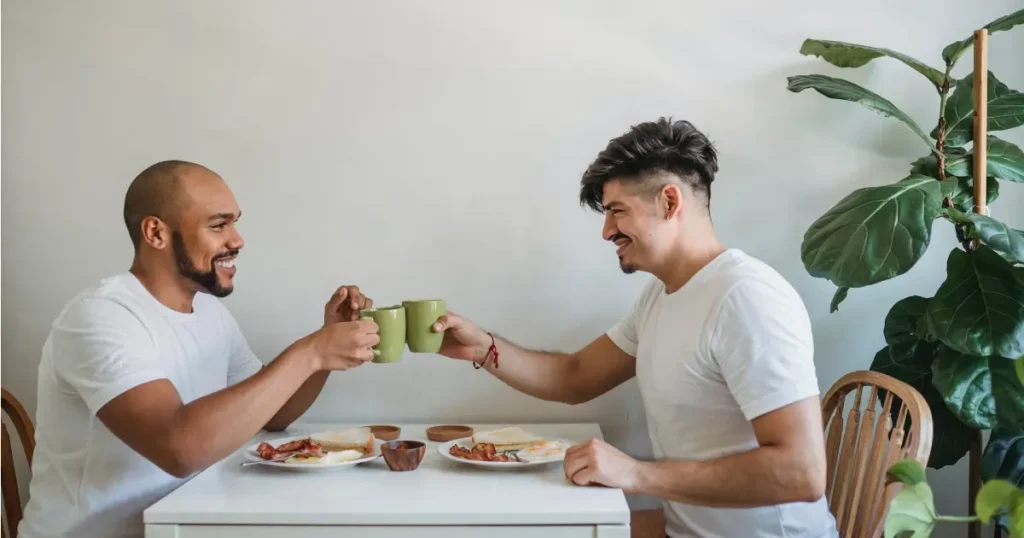 Dois homens sentados em uma mesa brindando com xícaras de café representando uma União Estável Homoafetiva