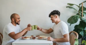 Dois homens sentados em uma mesa brindando com xícaras de café representando uma União Estável Homoafetiva