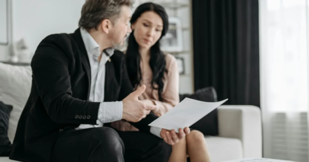 Homem de terno sentado segurando um papel falando com uma mulher mostrando uma folha de papel representando Inventário judicial e inventário extrajudicial