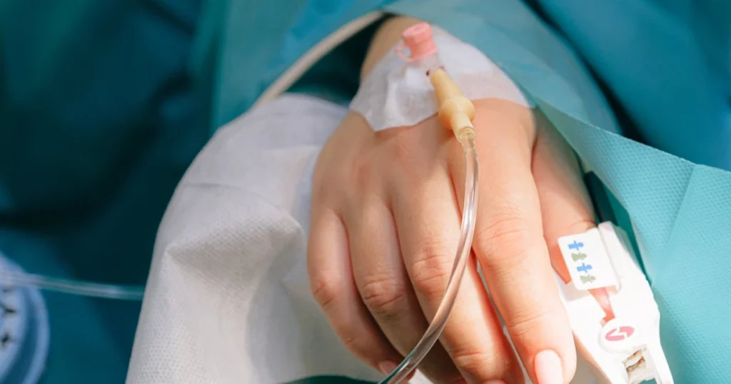 Mão feminina com um acesso de soro inserido representando o auxílio-doença